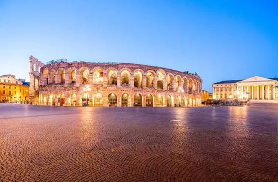 Verona's Roman Arena lit up at dusk above the empty cobblestone Piazza Bra
